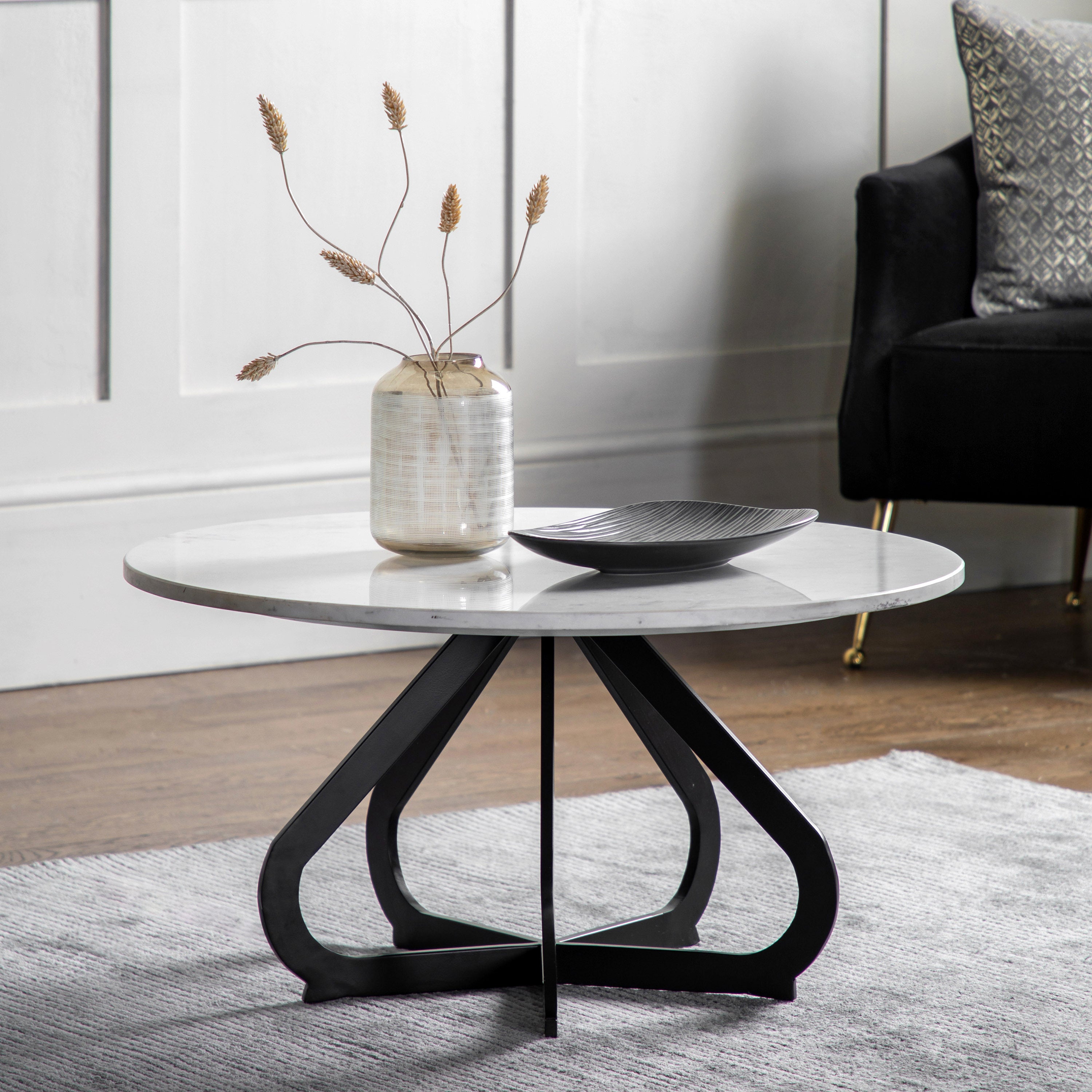 Round marble coffee table with black metal legs in a living room setting.