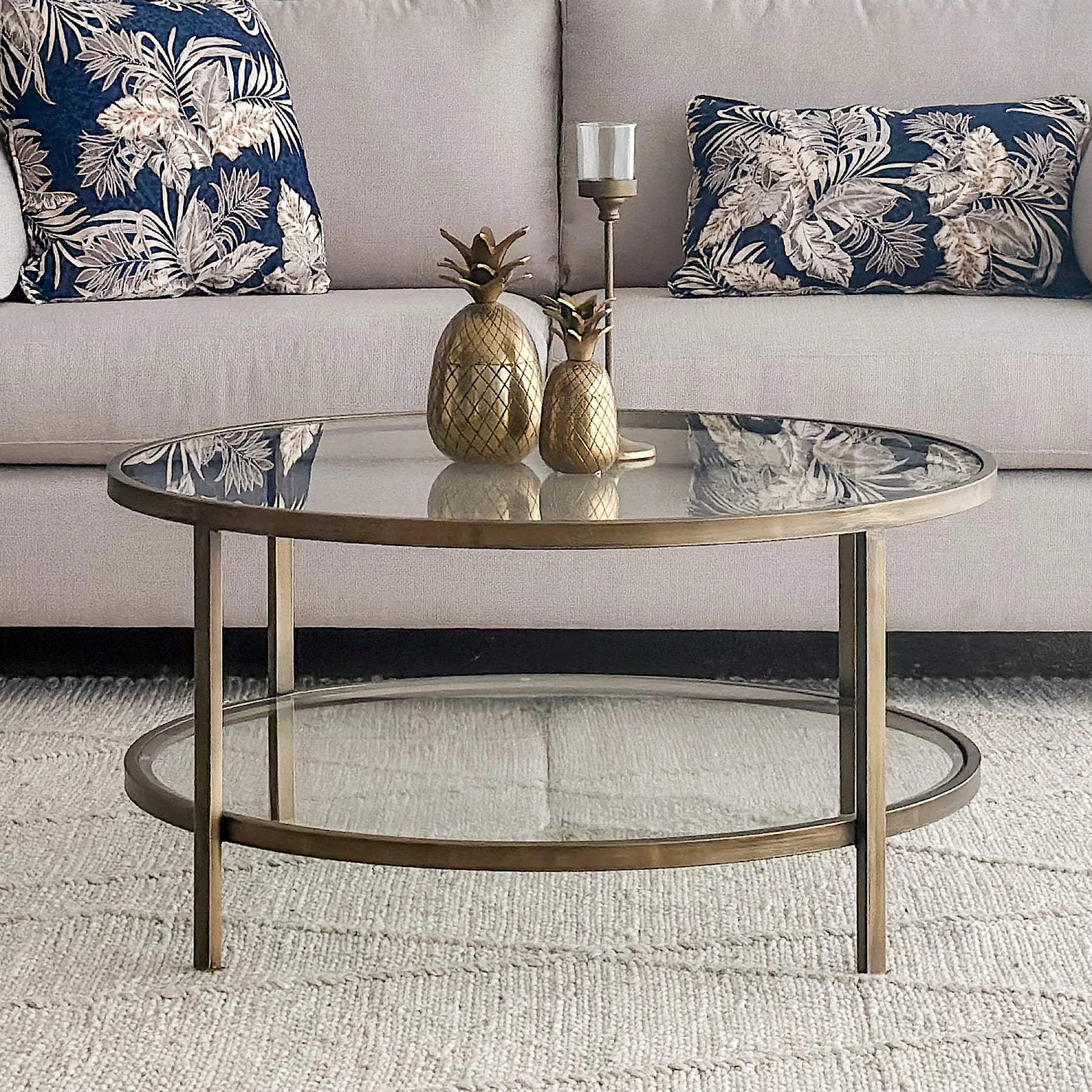 Round glass coffee table with gold metal base in a living room setting.