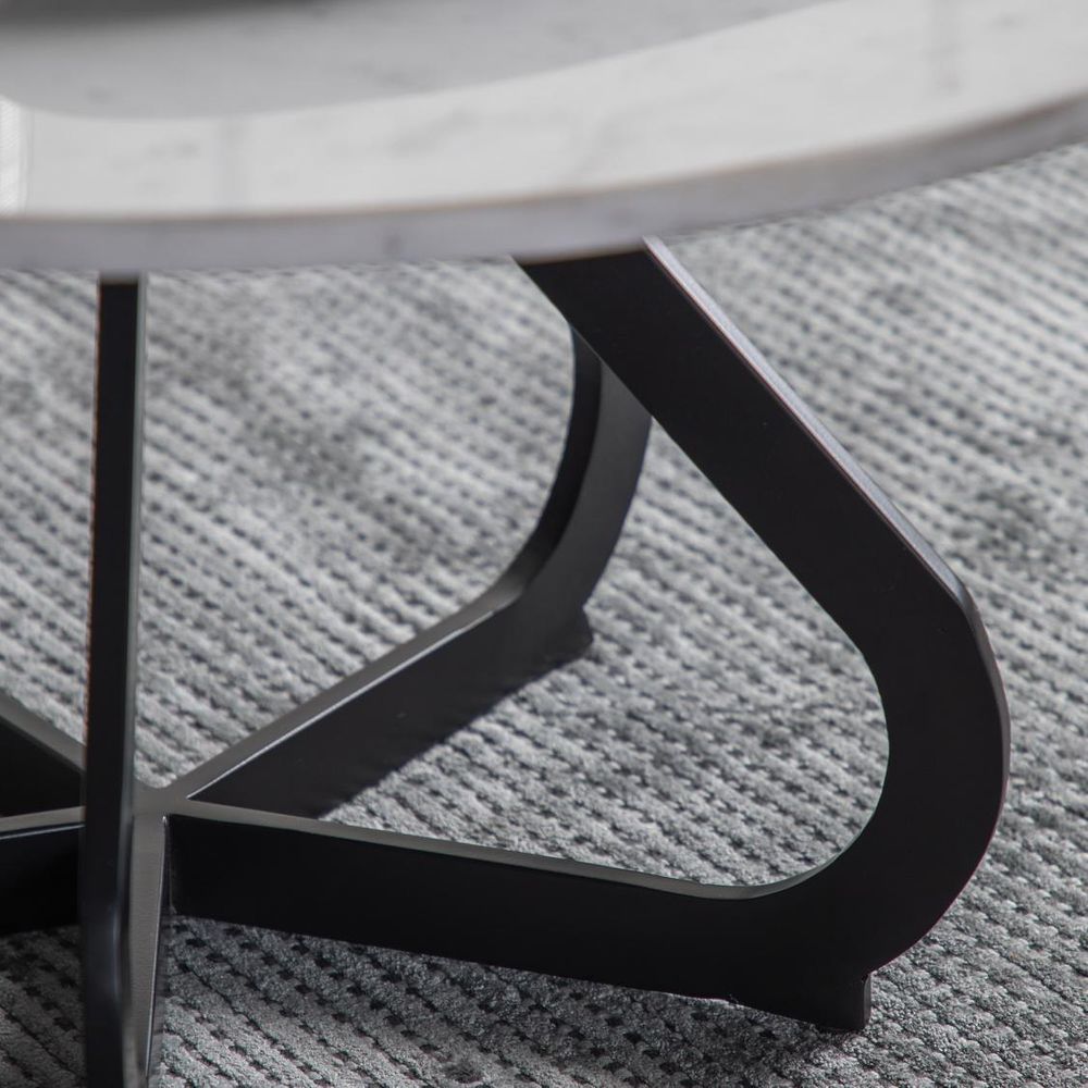 Close-up of a round marble table with a black metal base on a textured gray surface.